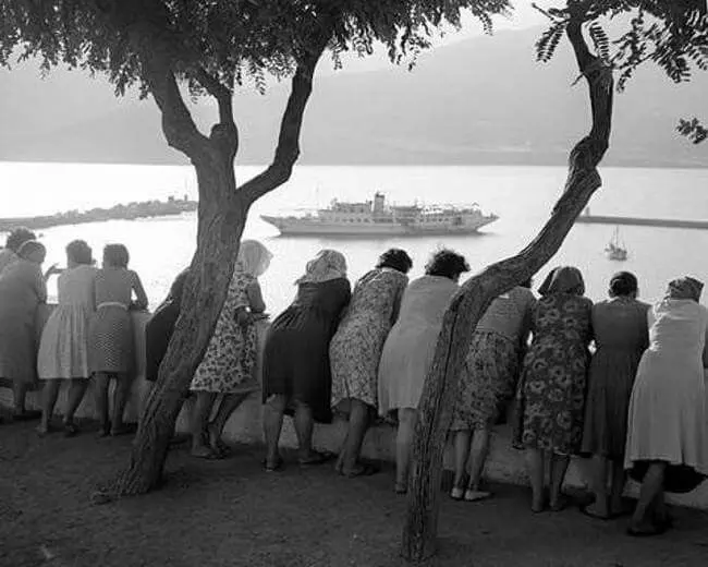 Old black-and-white photograph of women leaning on a wall to watch a ship in the harbour